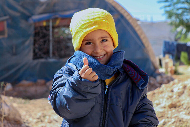 Bub aus Syrien trägt Winterkleidung und zeigt einen Daumen nach oben.