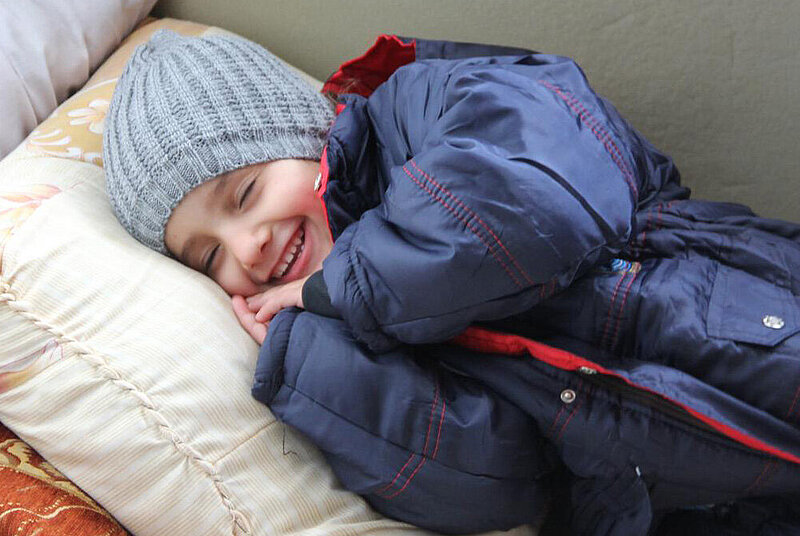 Kind schläft und lächelt und trägt Winterjacke.