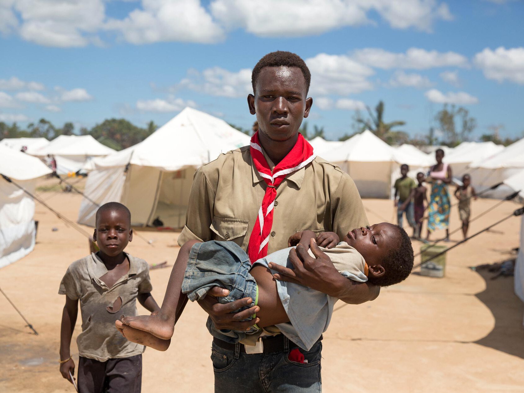 Freiwilliger Mitarbeiter trägt Flüchtlingskind mit Malaria in Mosambik.