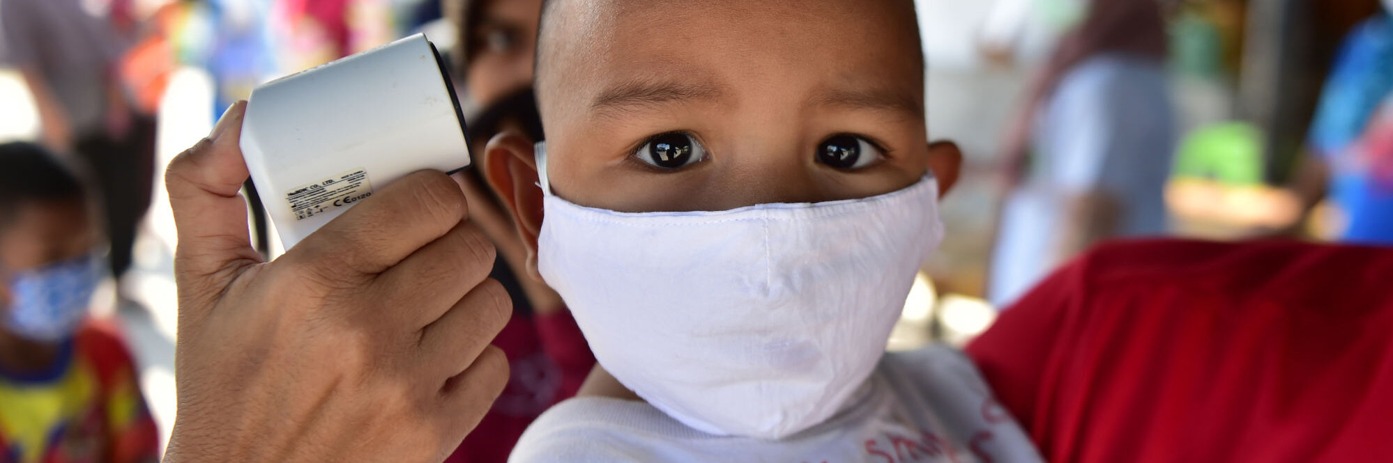 Bub in Thailand  trägt eine Maske gegen das Coronavirus, während Fieber gemessen wird. 