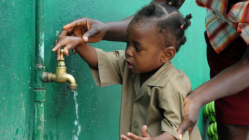 In Jamaika zeigt eine Lehrerin einem kleinen Buben, wie er einen Wasserhahn bedient.