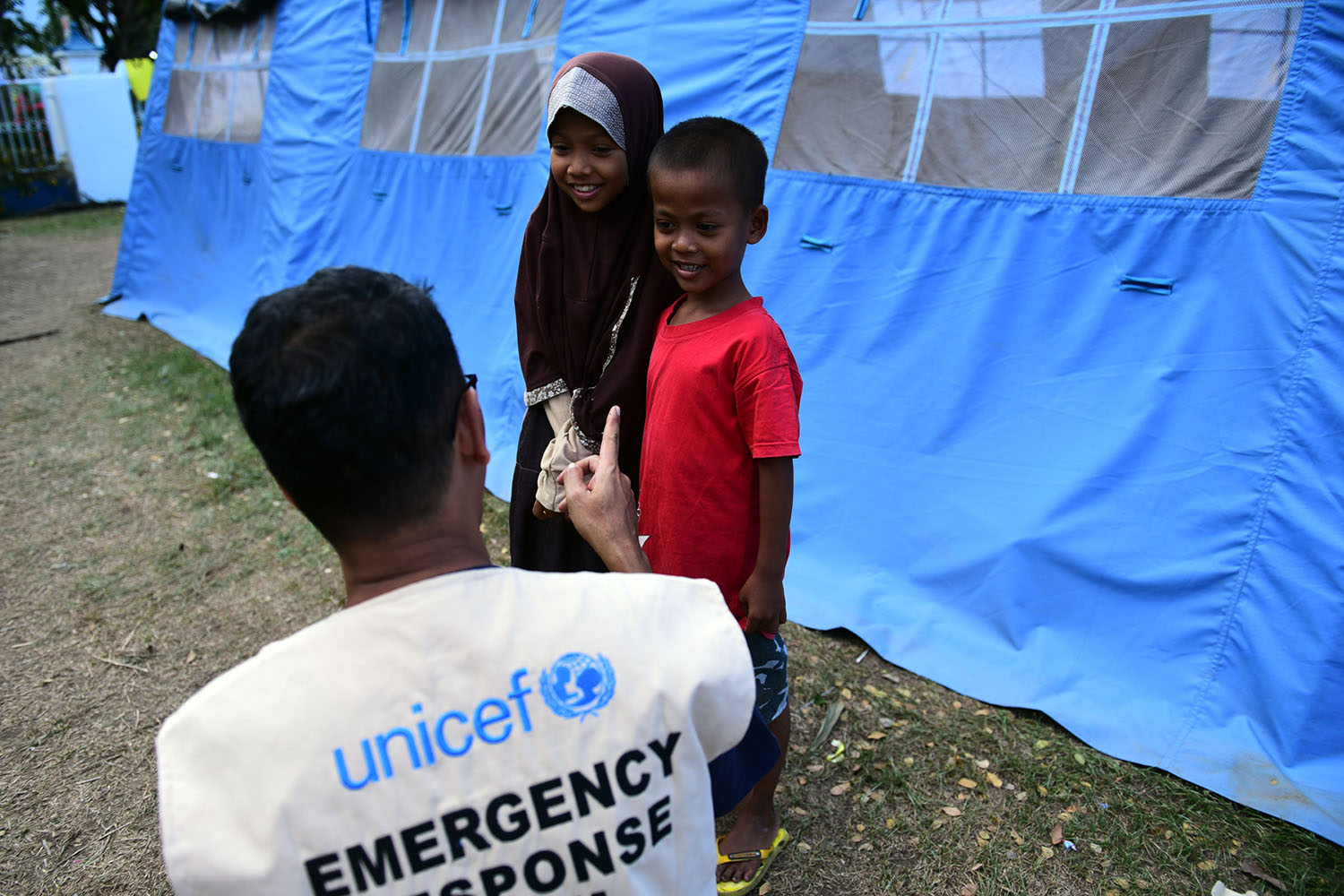 Ein UNICEF Mitarbeiter spricht mit zwei Kindern vor ihrem Zelt.