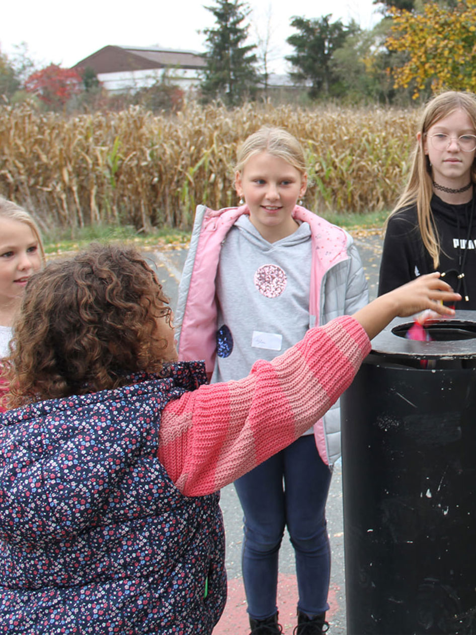 Kinder schmeißen Müll in eine Mülltonne.