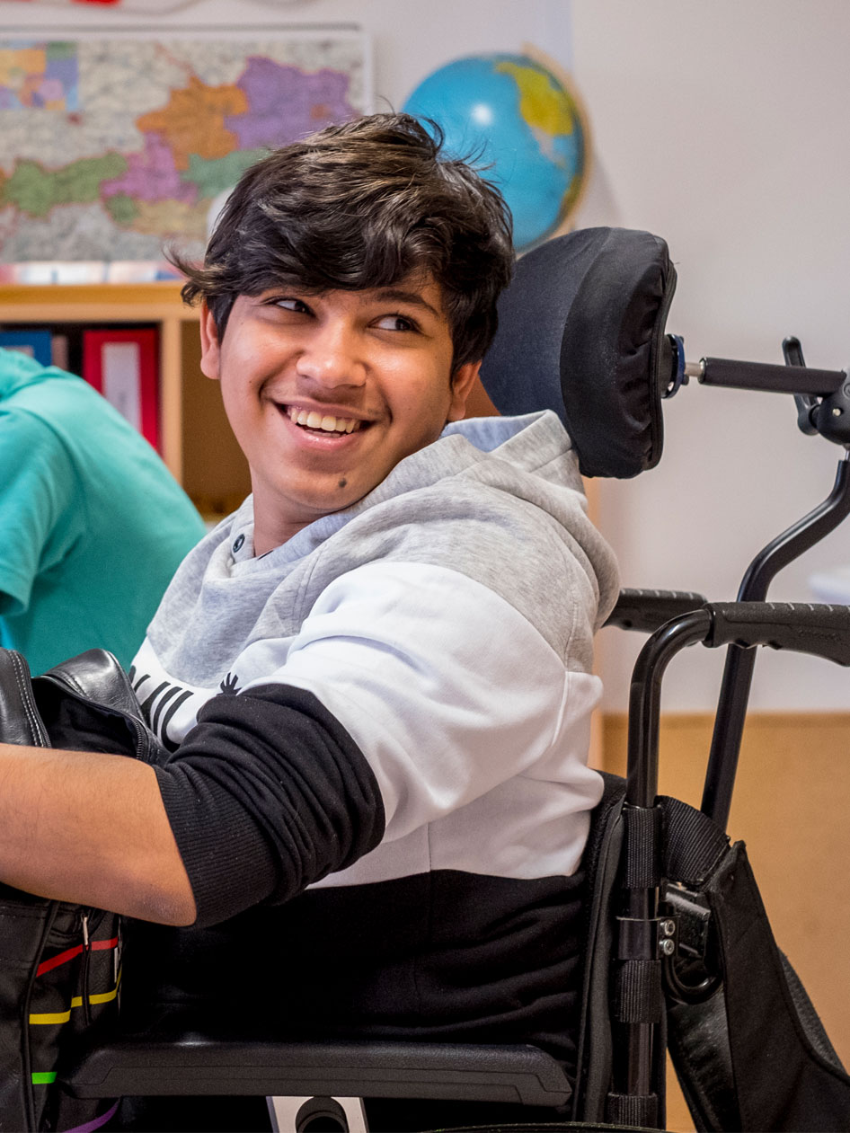 Sajad sitzt in einem Rollstuhl in seiner Klasse in Wien und lacht. 