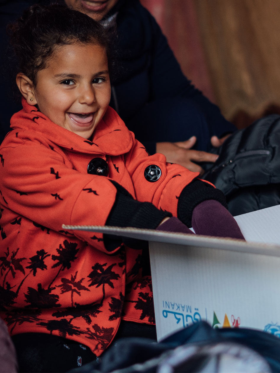 Lara aus Jordanien päckt warme Kleidung und Decken aus einem UNICEF Karton aus und lächelt dabei.