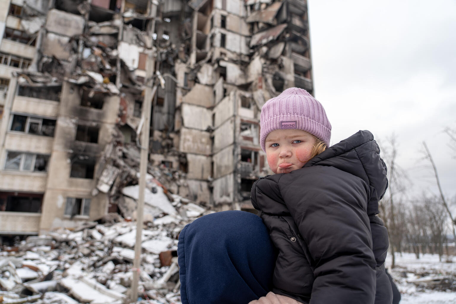 Ein kleines Mädchen sitzt auf den Schultern von ihrem Vater vor Trümmern. 