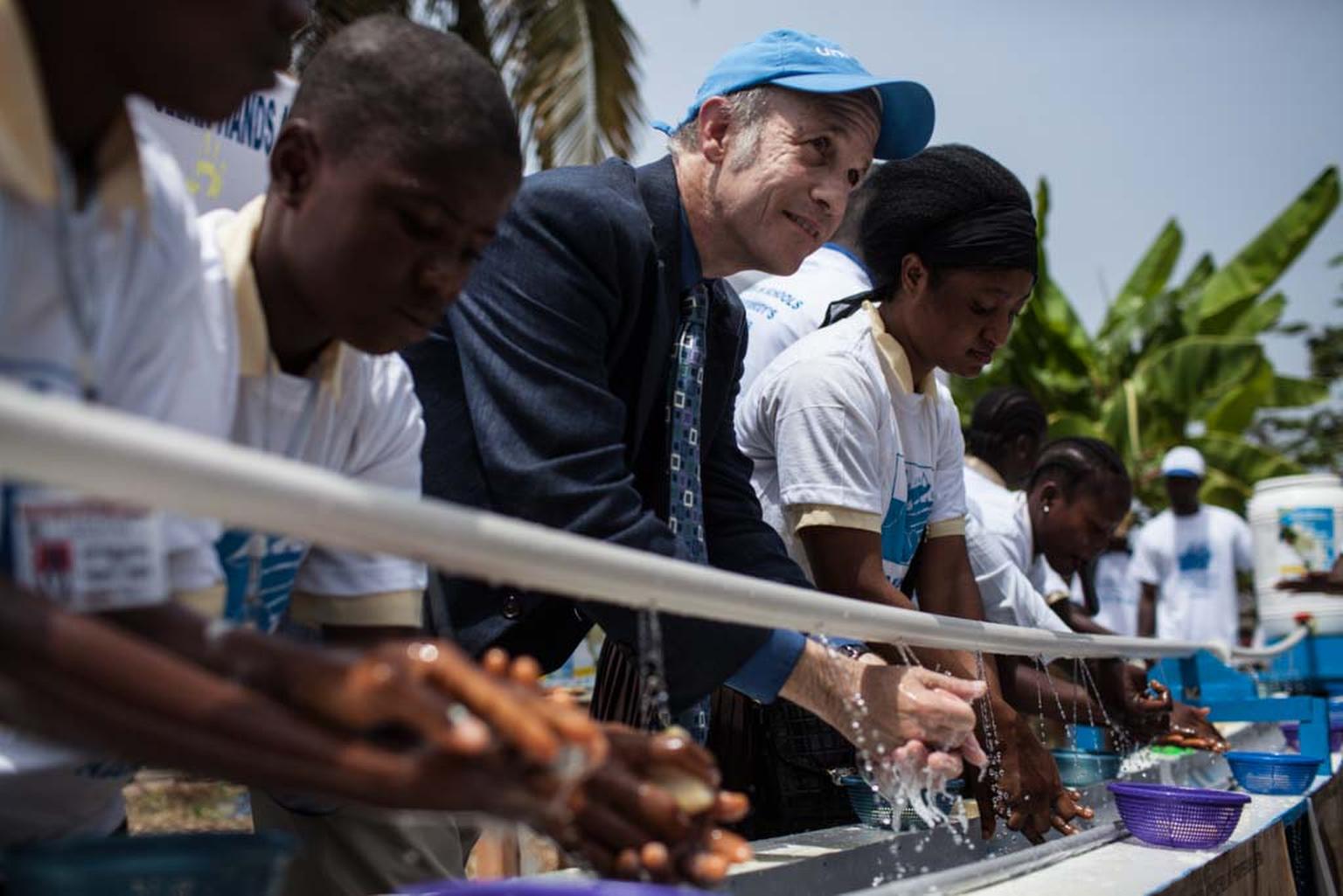Kinder und ein UNICEF Botschafter verwenden die Wasserstelle.