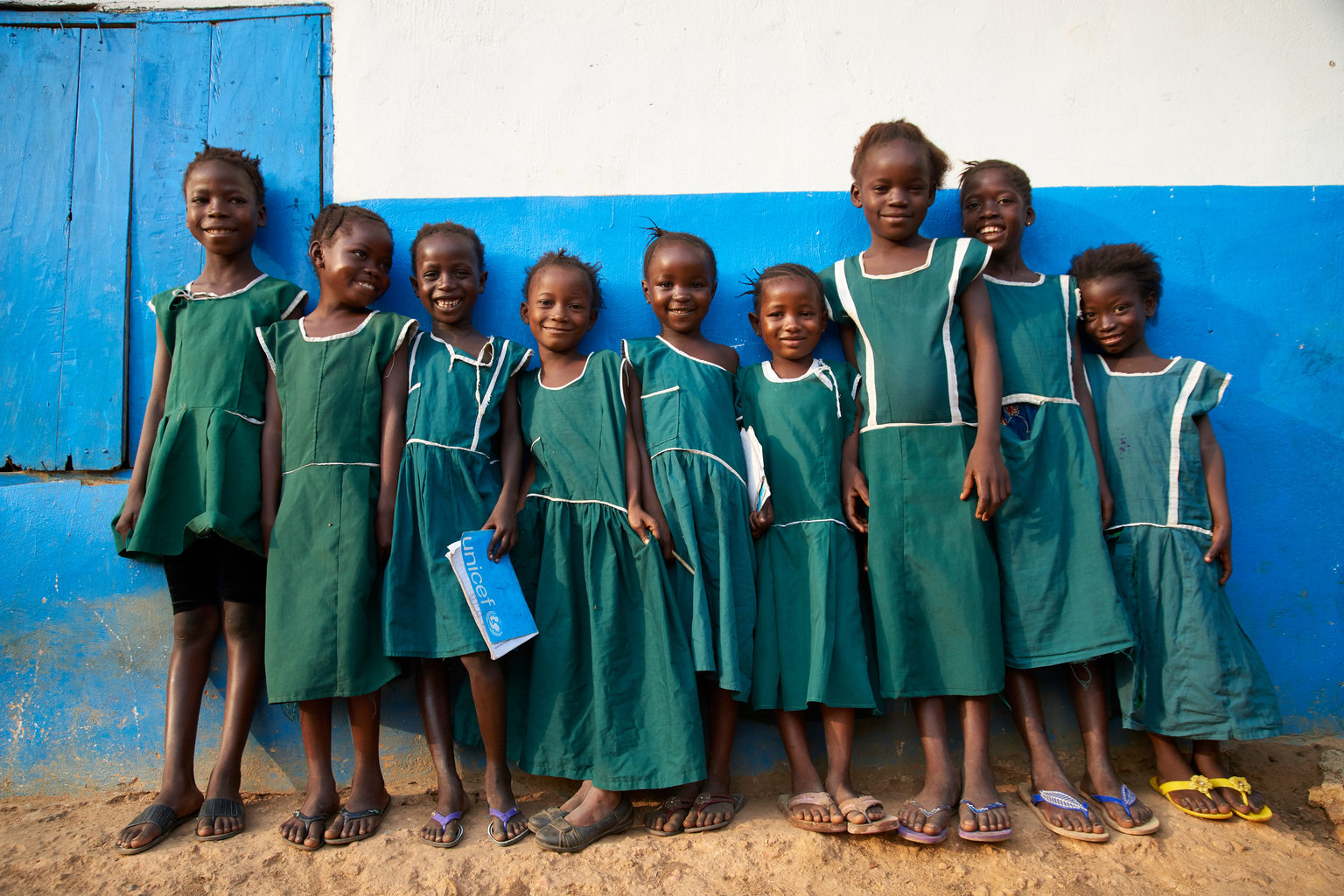 Neun Mädchen stehen vor ihrer Schule und lächeln zufrieden.