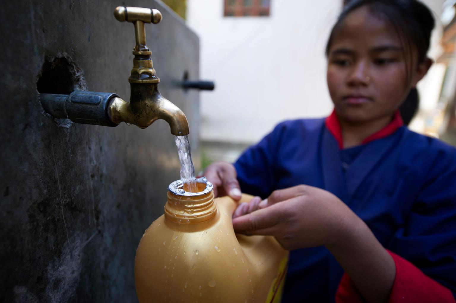 Ein Mädchen holt sich frisches Wasser von einem Brunnen.