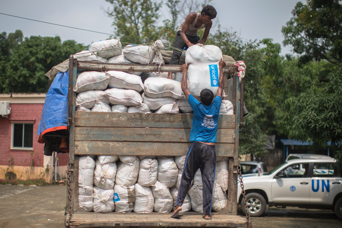 Drei UNICEF Mitarbeiter stapeln Säcke mit Hilfsgütern auf einem Truck.