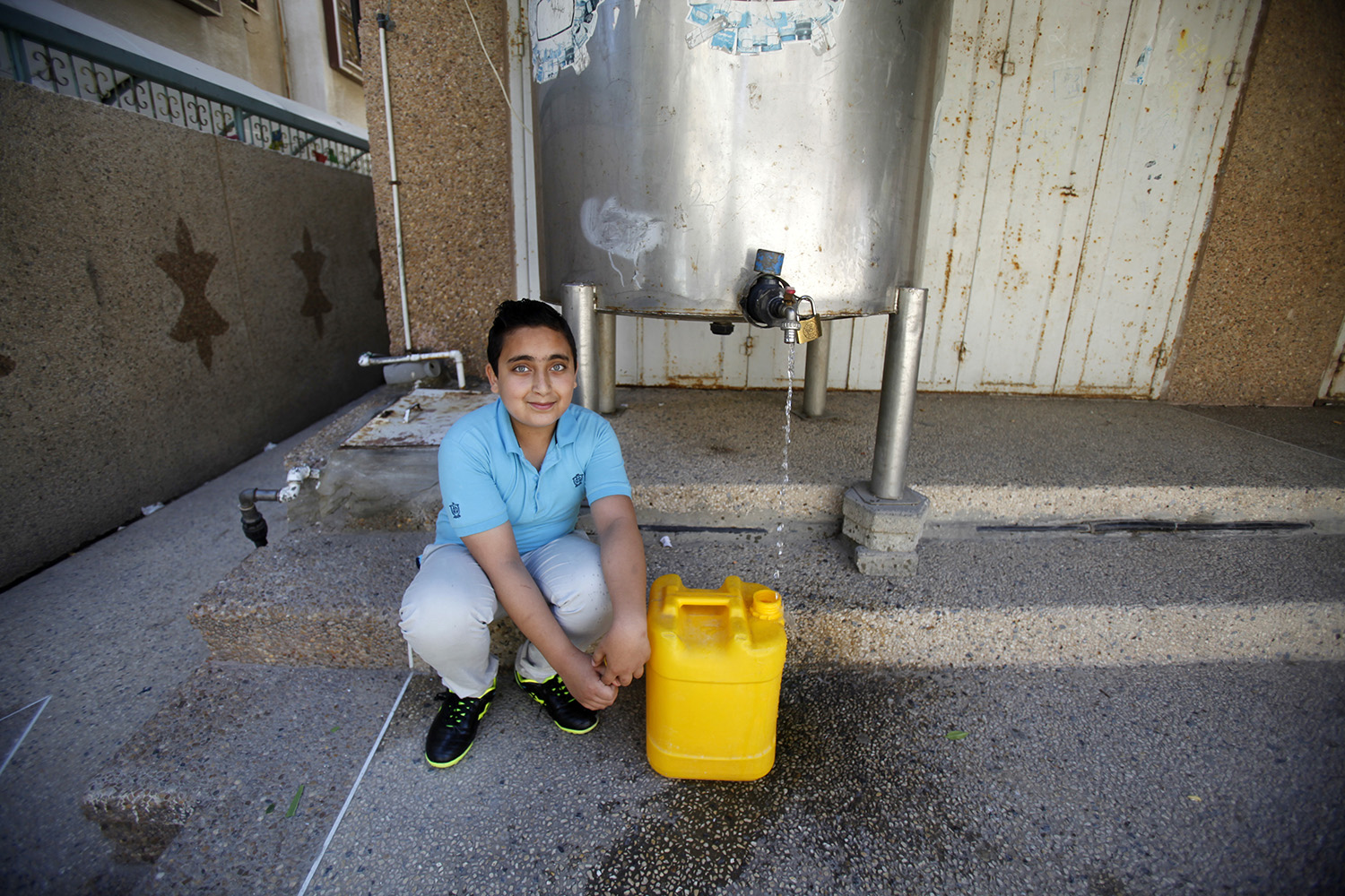 Ahmed füllt einen Kanister ab und hockt neben dem Wassertank.