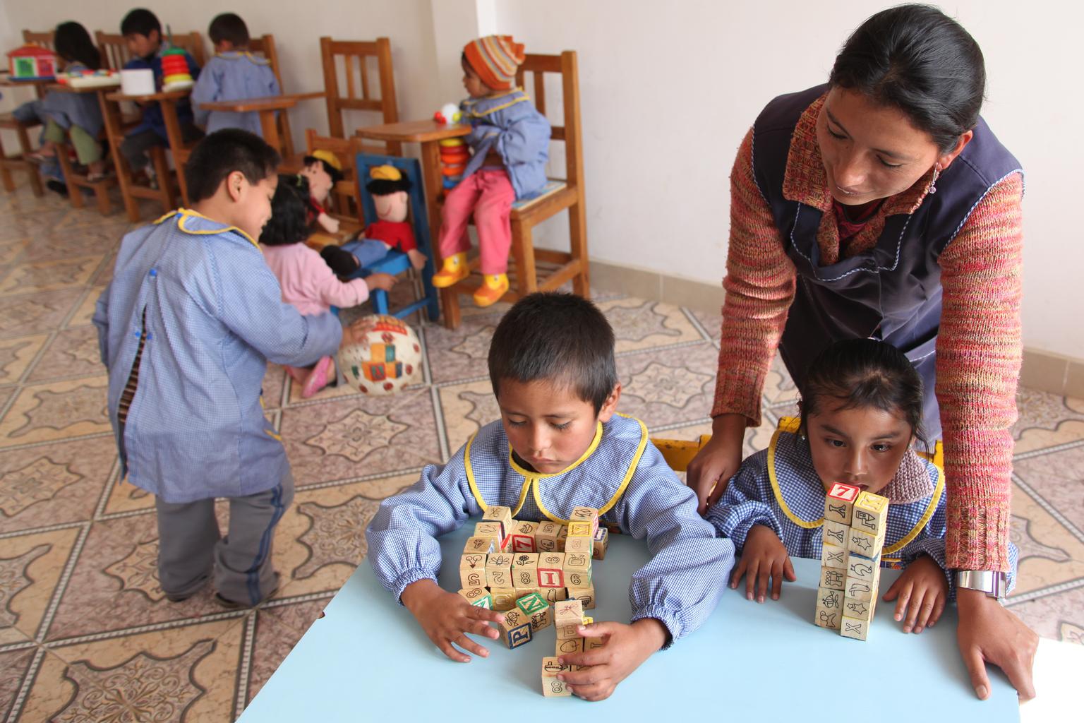 Zwei Kinder spielen mit Holzblöcken, die Betreuerin hilft ihnen.