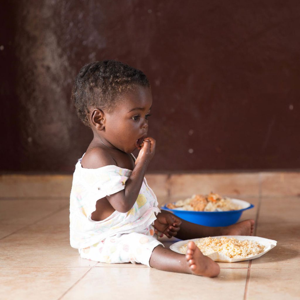 Kind sitzt am Boden und isst therapeutische Nahrung