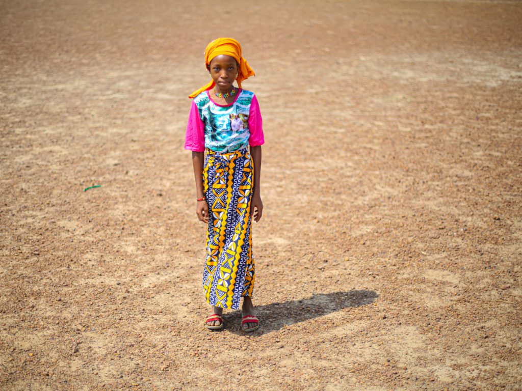 Ein Mädchen in Mali steht auf Wüstenboden.