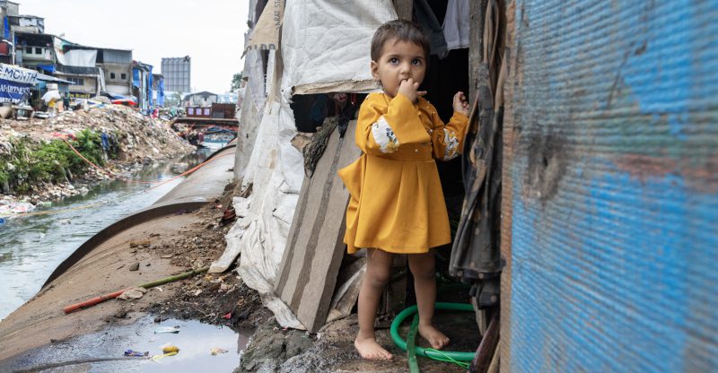 Ein indisches Mädchen in einem Slum steht vor ihrem Zelt.