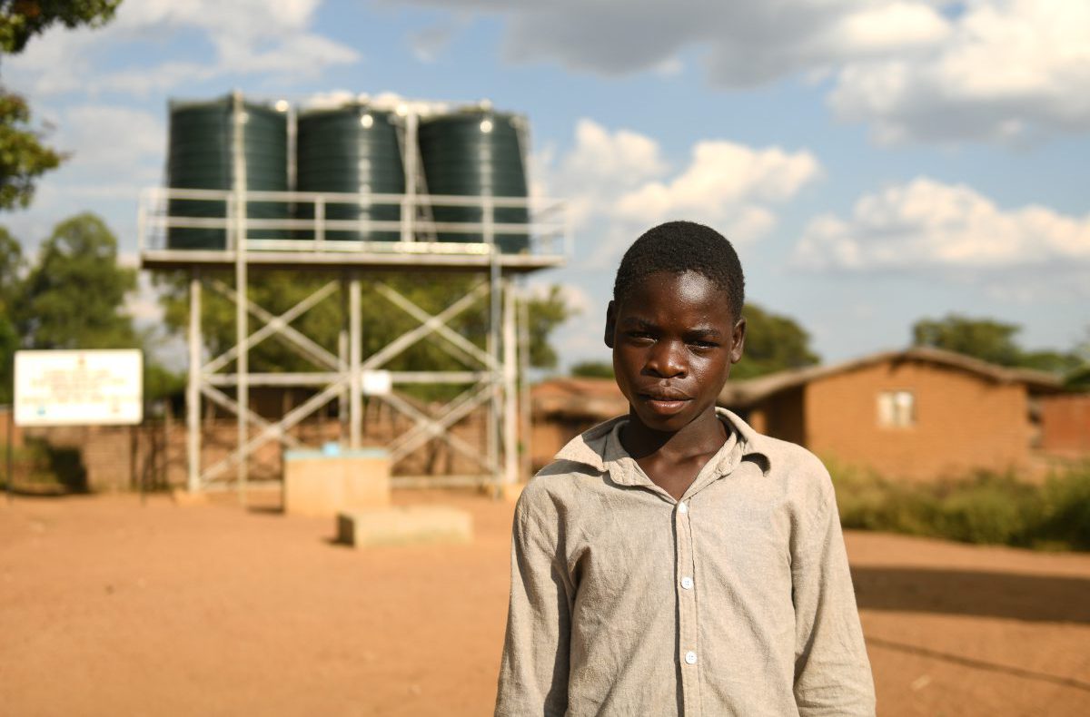 Junge in Malawi steht vor einer solarbetriebenen Wasserpumpe.