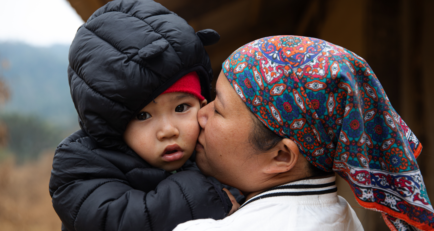 Mutter hält ein Kind mit einer dicken Winterjacke in Vietnam.