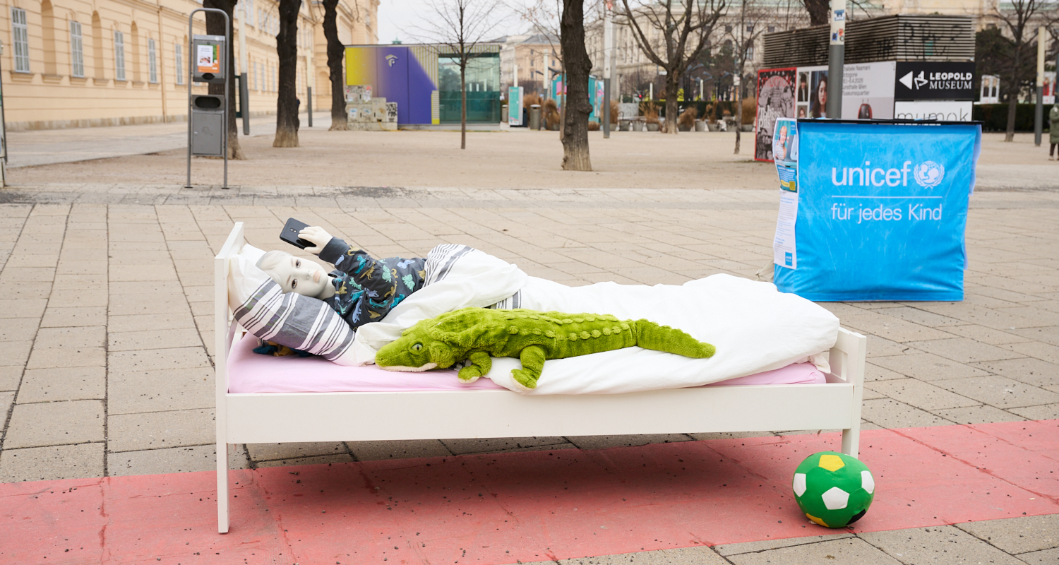 Puppe eines Kindes liegt in einem Bett auf der Straße und scrollt auf einem Handy.