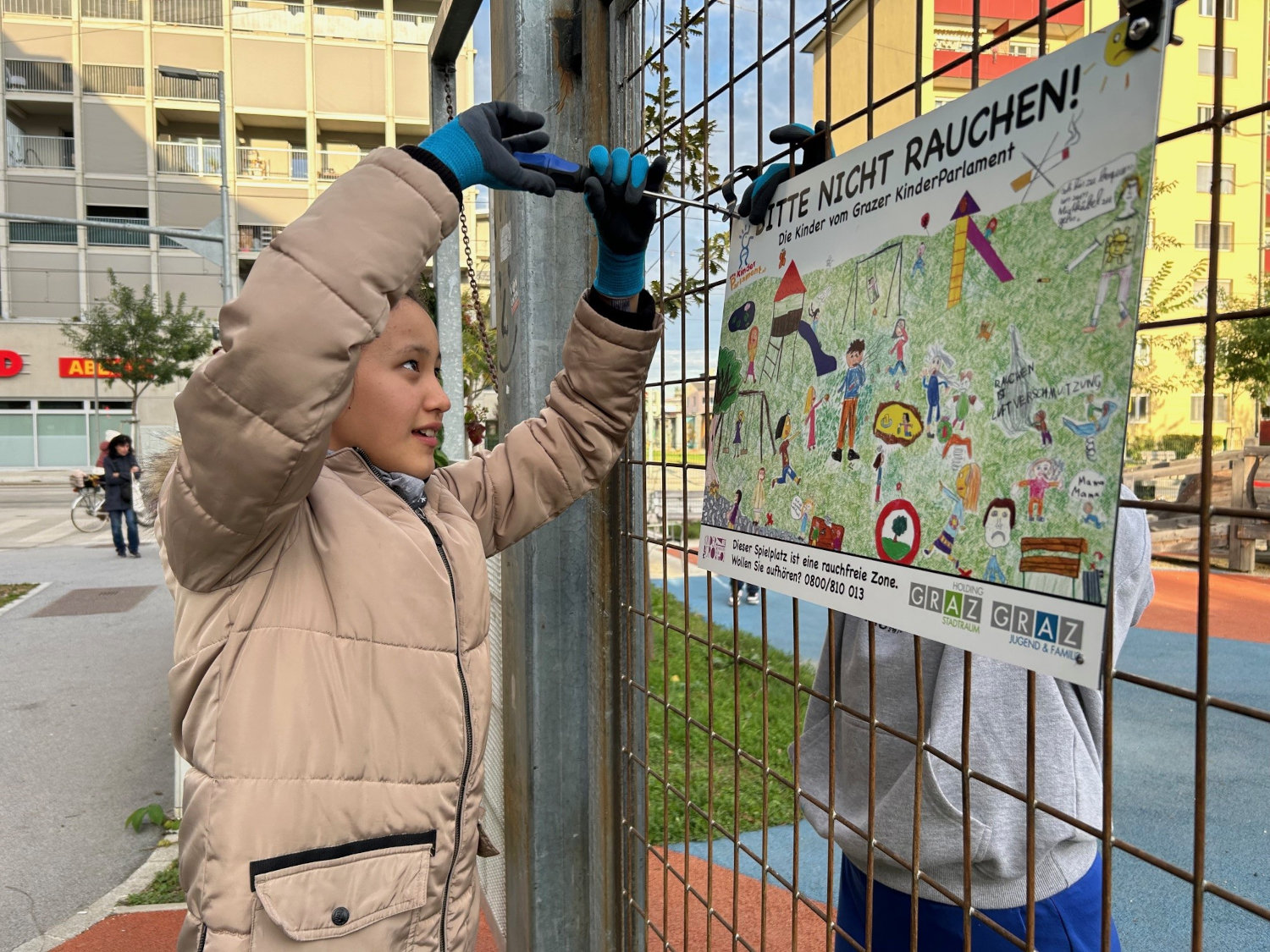 Ein Mädchen montiert die Verbotstafel am rauchfreien Spielplatz.