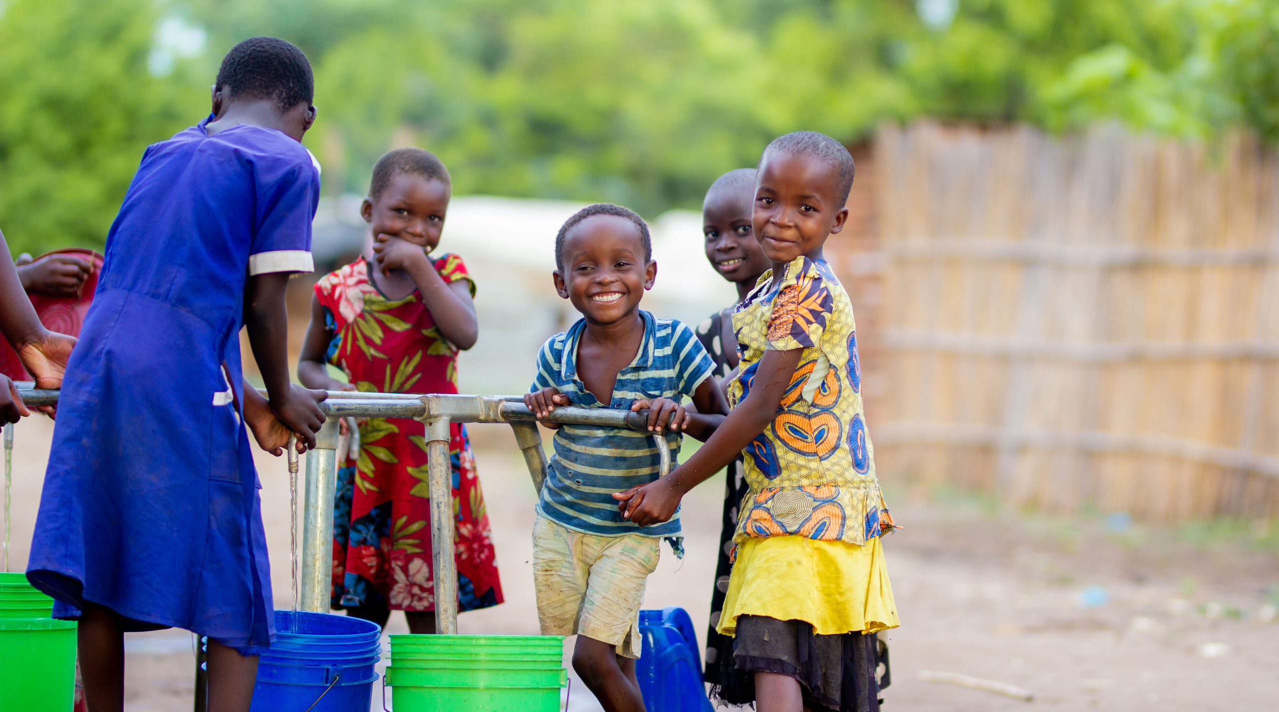 Kinder holen Wasser von einer Trinkwasserpumpe