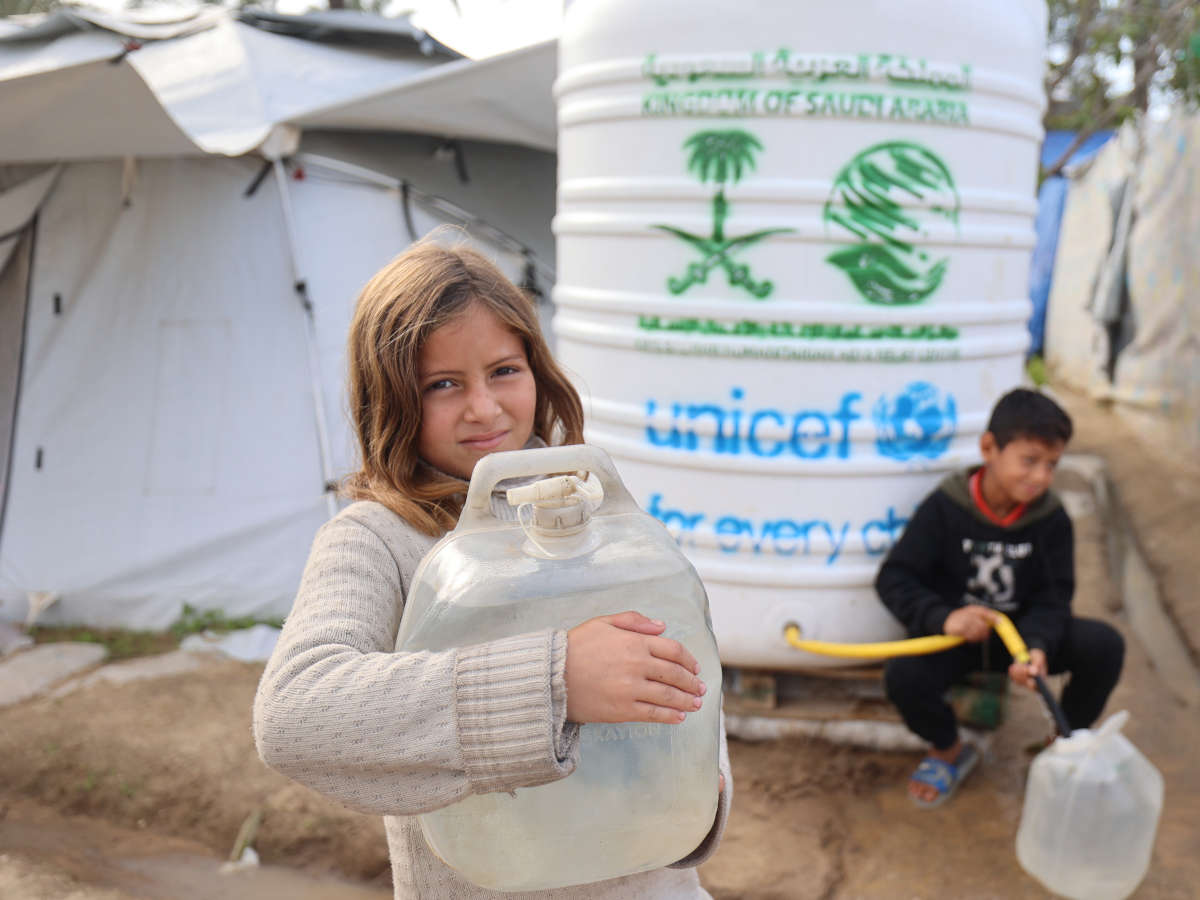 Ein Mädchen und Junge vor einem UNICEF-Wassertank in einem Flüchtingscamp in Gaza.