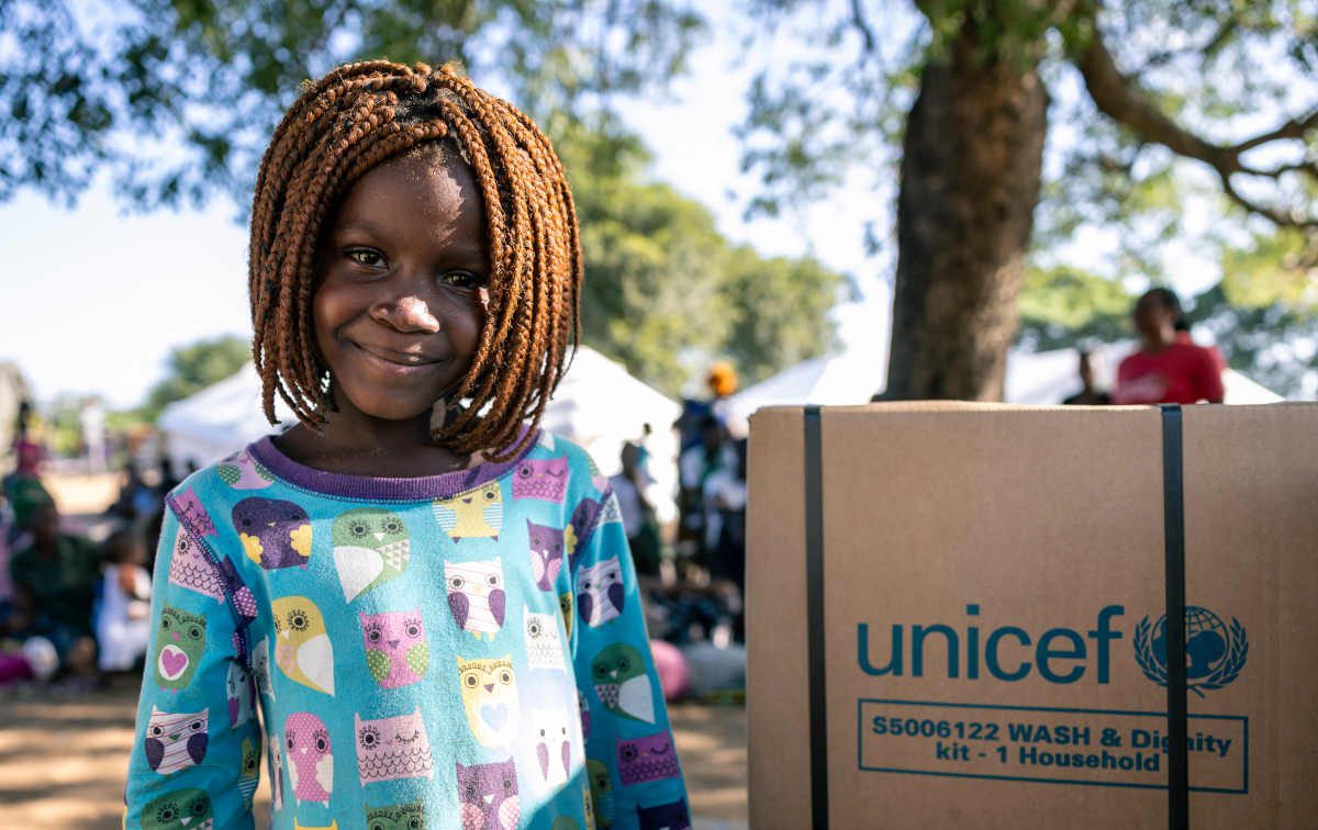 Mädchen in Mozambique mit UNICEF-Paket lächelt freundlich.
