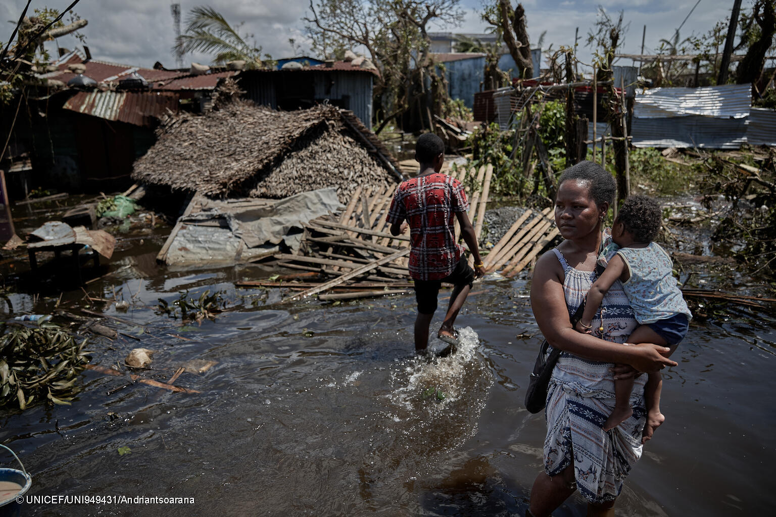 Drei Menschen waten durch ein überschwemmtes Gebiet in Madagaskar.