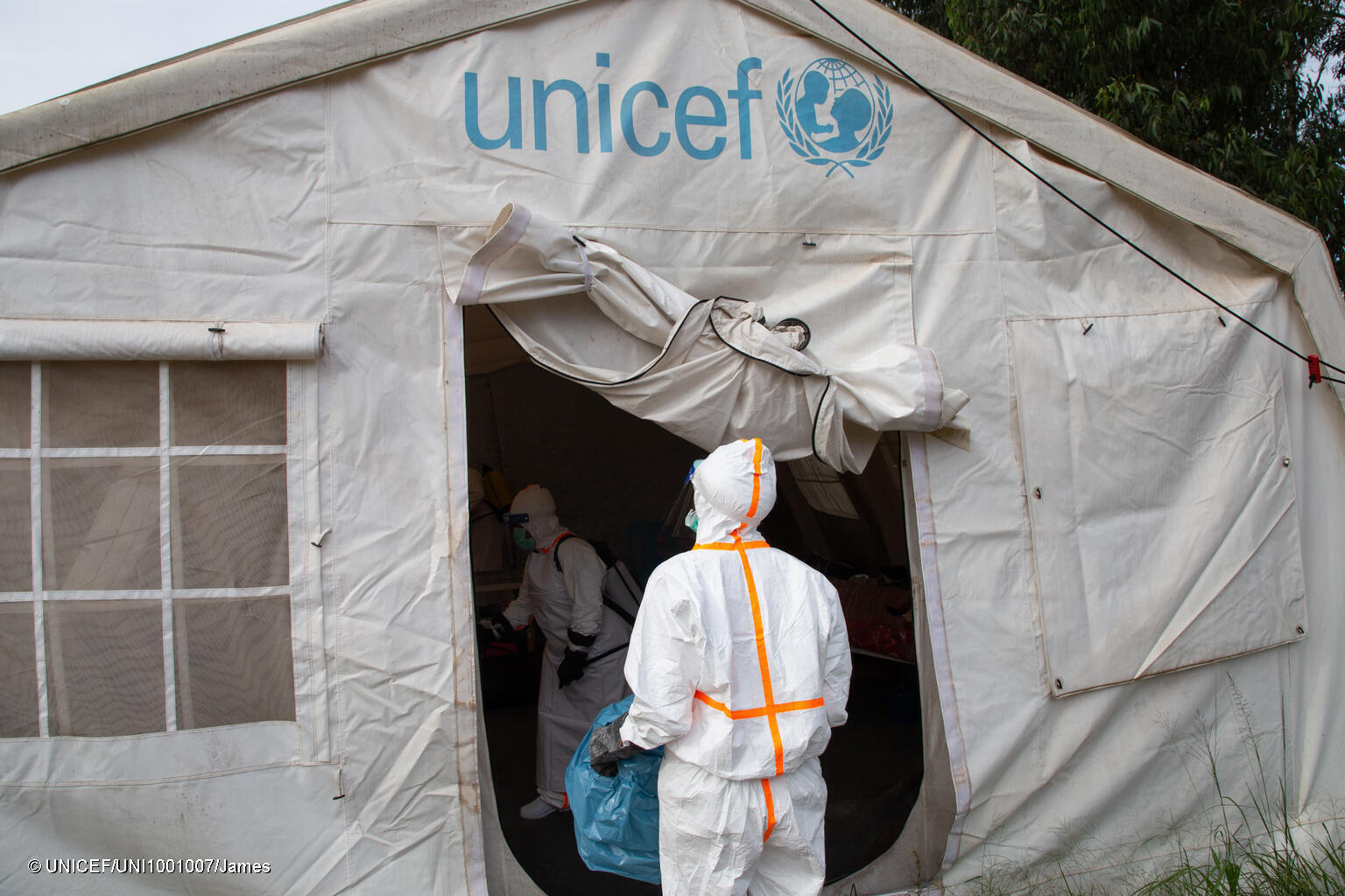 In einem UNICEF Zelt stehen Menschen in Schutzanzügen.